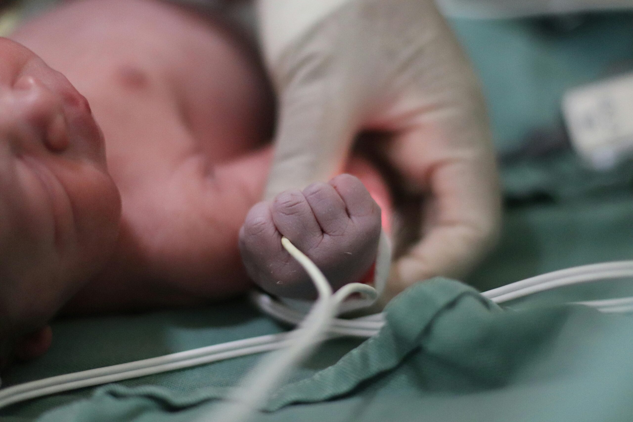 Close-up of a newborn baby's hand being held by a healthcare professional in a hospital environment.